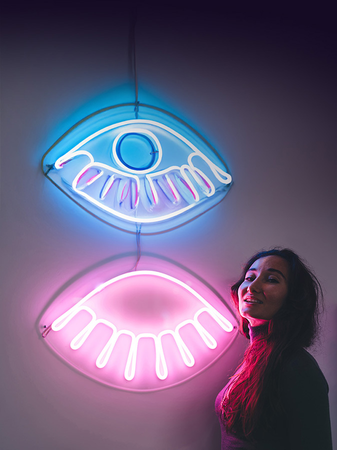A woman standing next to two neon eyes