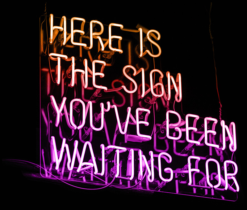 A neon sign with the words "here is the sign you've been waiting for"